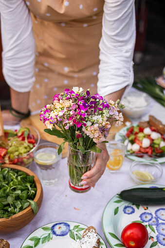 Woman arranging dining table with bouquet of flowers. Setting table for garden party