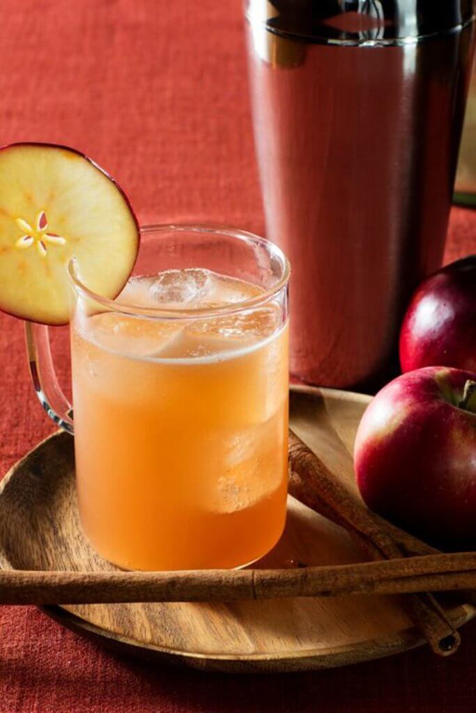 caramel apple mule with an apple garnish set on a bamboo plate, decorated with cinnamon sticks and an apple