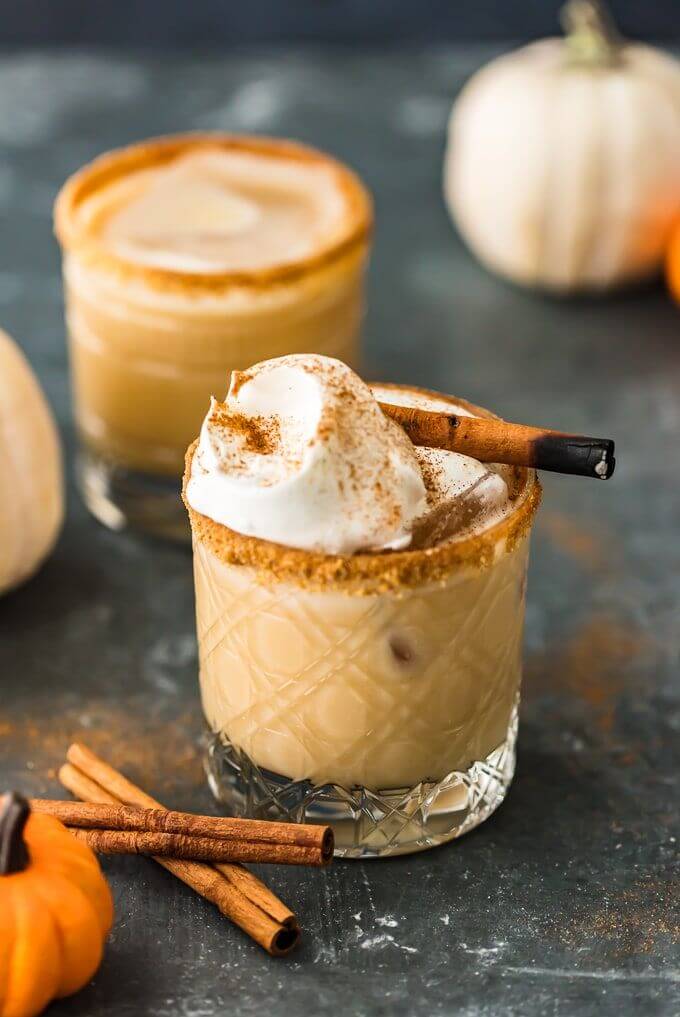pumpkin white Russian in a cinnamon rimmed glass, with cinnamon sticks and pumpkins in the background