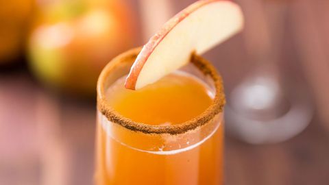 apple cider mimosa in a champagne flute with a cinnamon rim and an apple garnish