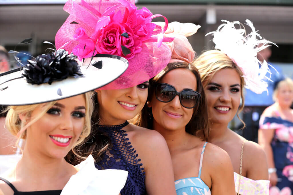 Women wearing brightly colored hats on a sunny day at the track