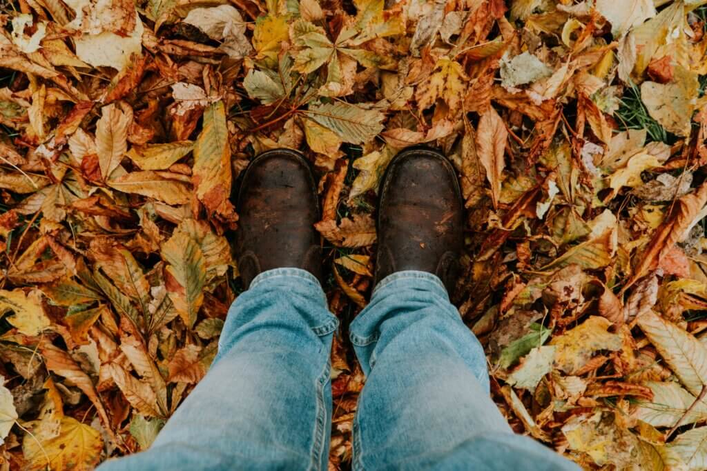Two feet in leather boots standing on a pile of leaves