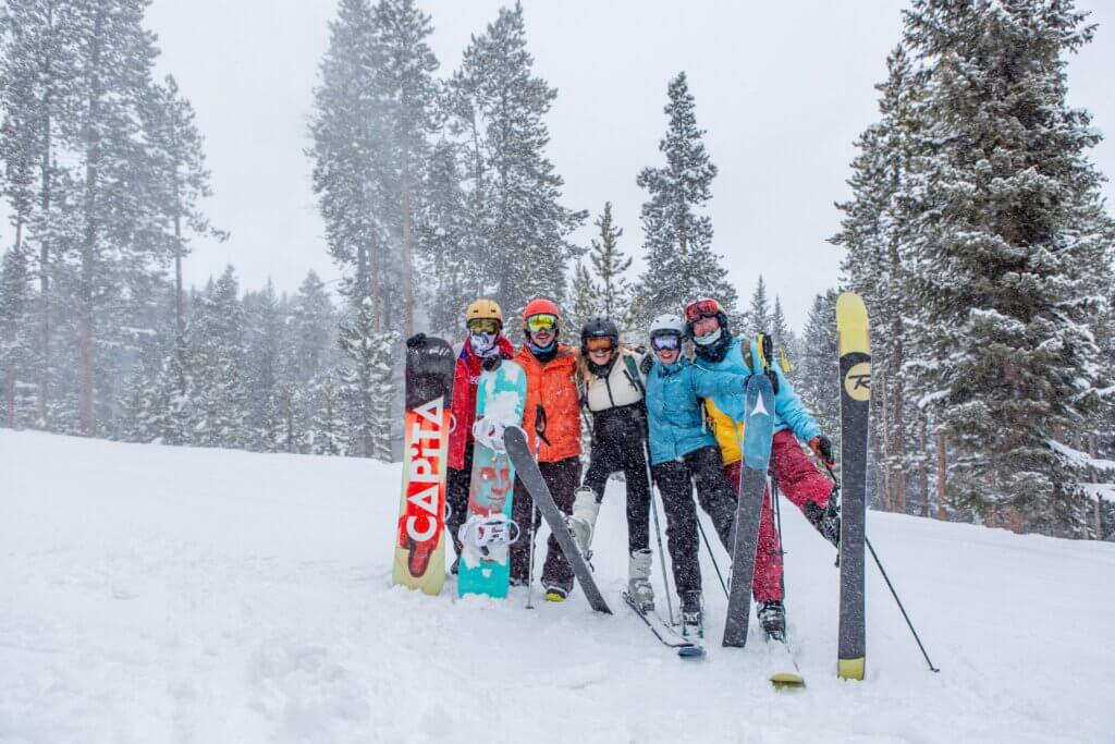 Group of friends standing in the snow with skis and snowboards