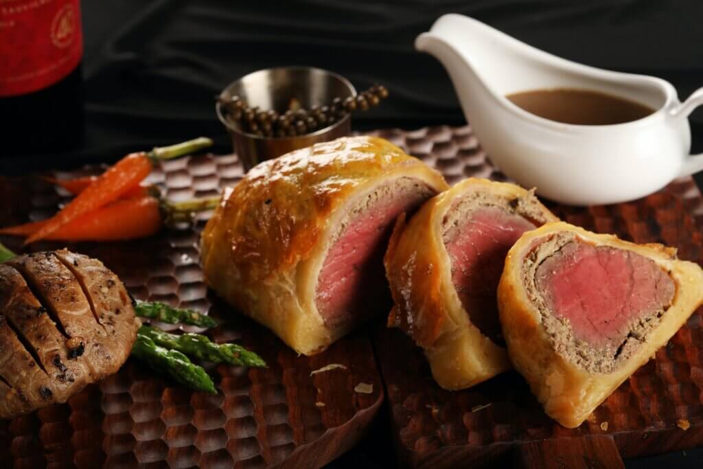 Beef wellington on a tray with gravy and vegetables