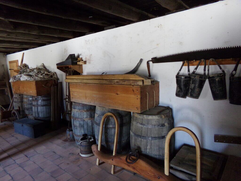 Building interior with preserved barrels, pails, saw, and other colonial-era tools