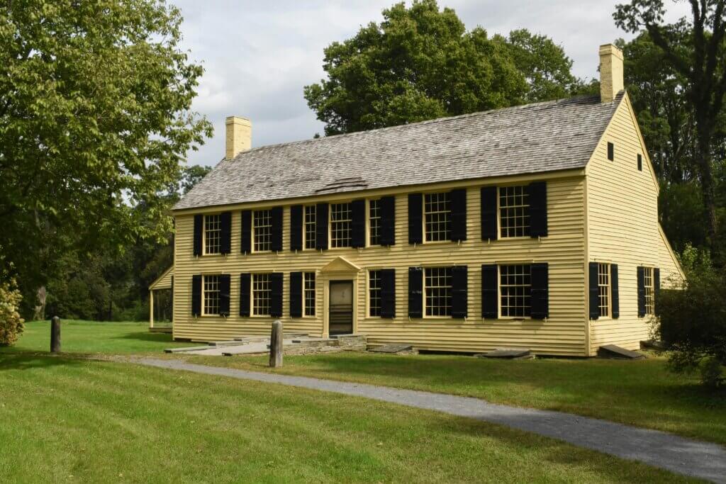 Yellow colonial home surrounded by green trees and grass